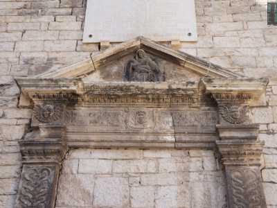 Ne osserviamo l�architrave triangolare finemente scolpita con teste alate a incorniciare l�epigrafe centrale, su cui si impone il bassorilievo di Maria che regge in grembo il corpo esanime del figlio
